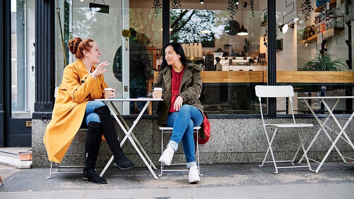 ASGF00369 - Woman gesturing while talking with female friend outside coffee shop