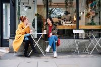 ASGF00369 - Woman gesturing while talking with female friend outside coffee shop
