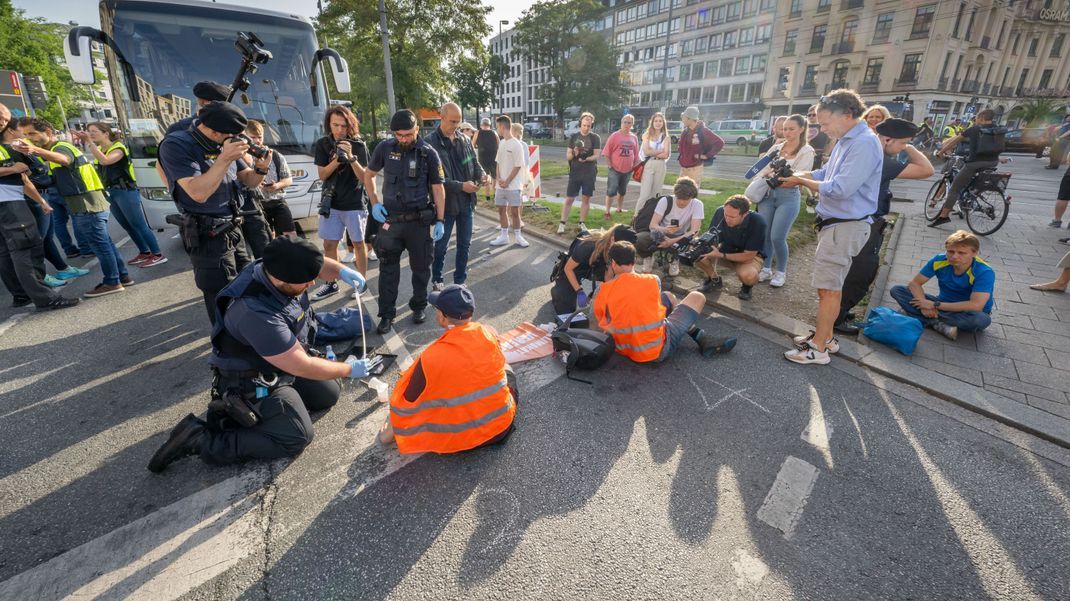 Polizisten versuchen auf der Kreuzung am Stachus Aktivist:innen der "Letzten Generation" vom Strassenbelag zu lösen.