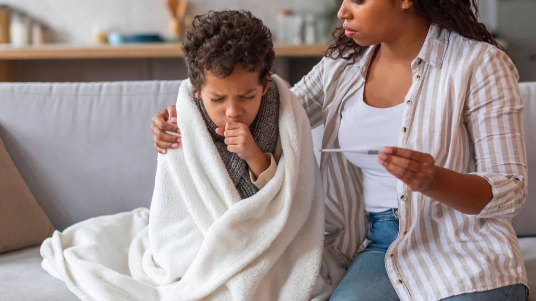 Worried black mother holding thermometer and looking at her coughing son