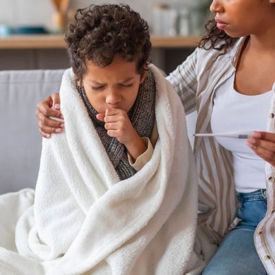 Worried black mother holding thermometer and looking at her coughing son