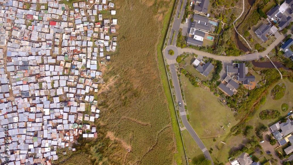 Mit Blick aufs Armutsviertel: So leben die Rentner:innen der Seniorenwohnanlage Evergreen Lake Michelle in Kapstadt, Südafrika.&nbsp;In der Gated Community lebt die weiße Bevölkerung strikt getrennt von der schwarzen. Elektrische Zäune, hohe Grenzmauern, strenge Zugangskontrollen und eine 24/7 Überwachung schotten sie von den Menschen des Townships Masiphumelele (bedeutet auf Xhosa "Lasst uns Erfolg haben") ab.&nbsp;