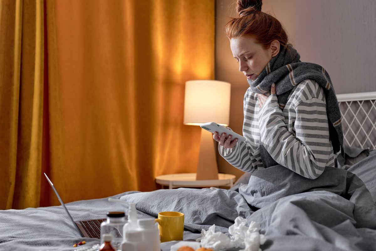 Frau sitzt krank im Bett und nutzt die Option der telefonischen Krankmeldung