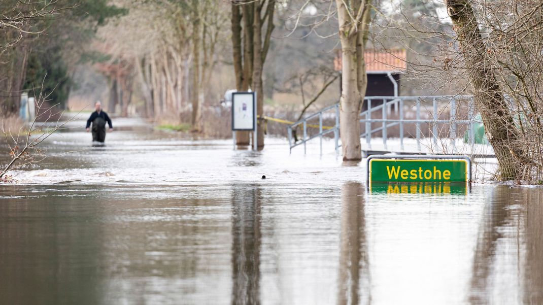 30.12.2023, Niedersachsen: Eine Person läuft auf einer überfluteten Straße in der Siedlung Westohe der Gemeinde Winsen (Aller) im Landkreis Celle, die am Fluss Aller liegt.