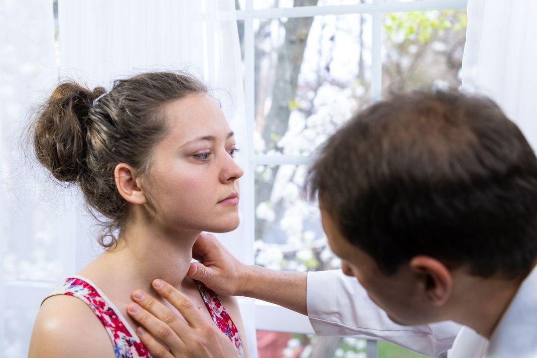 Arzt untersucht die vergrößerte Schilddrüse einer Patientin.