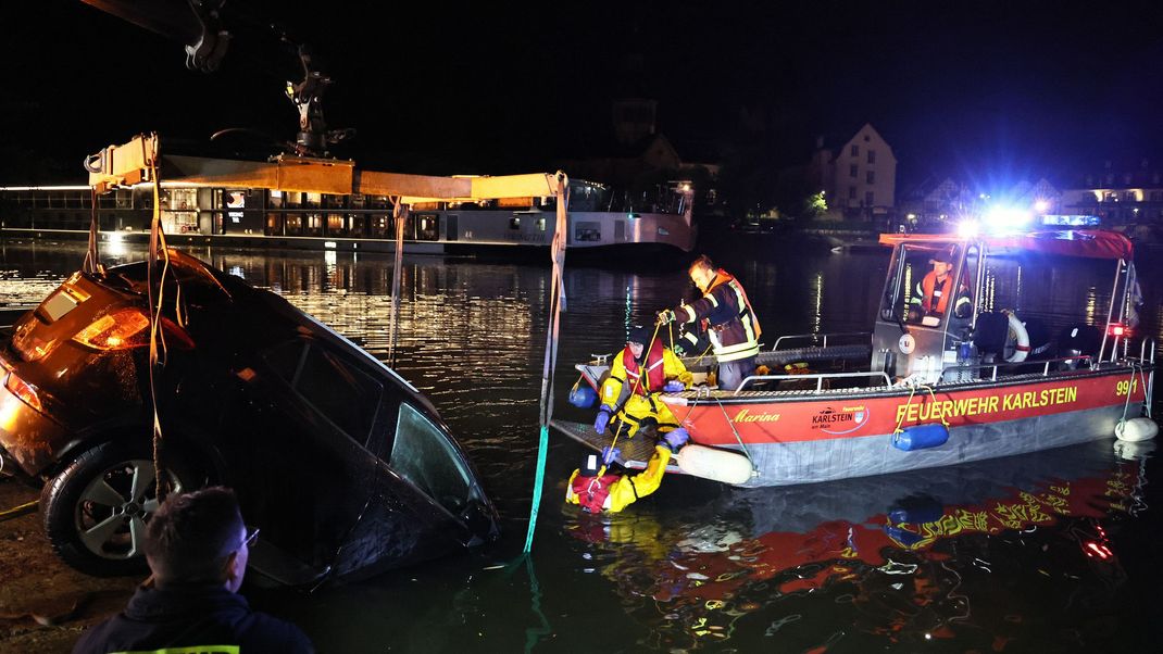 Die Feuerwehr birgt ein Auto, das mit dem vorderen Teil über eine Kaimauer gefahren und im Wasser gelandet ist.