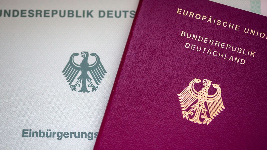 Eine Einbürgerungsurkunde der Bundesrepublik Deutschland (l.) und ein deutscher Reisepass liegen auf einem Tisch.