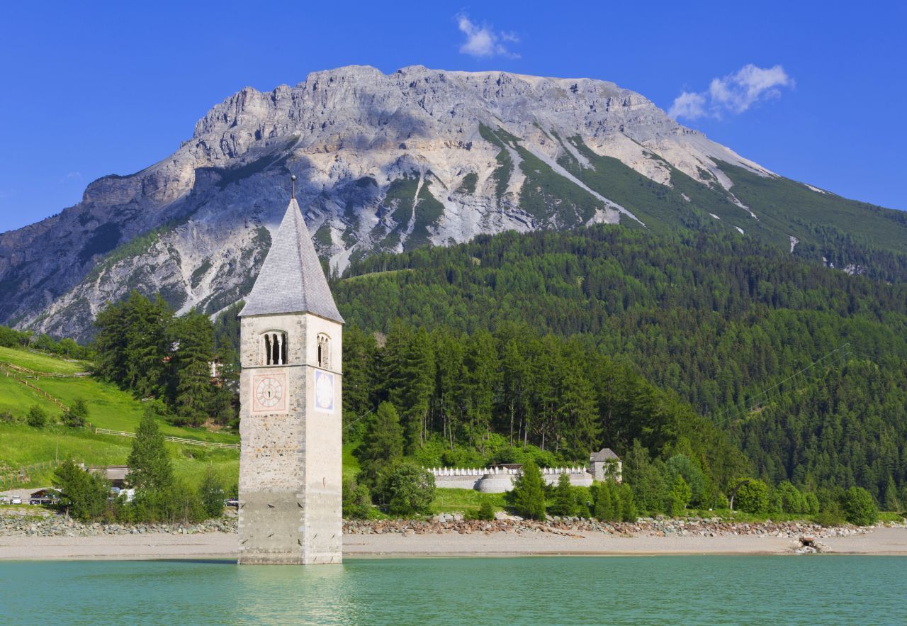 Alt-Graun, Italien: 1950 entschied die Regierung: Norditalien braucht einen Stausee, um sich über ein Wasserkraftwerk mit Strom zu versorgen. Also wurden die Naturseen von Graun und Reschen kurzerhand zu einem großen See aufgestaut – und das Dorf Alt-Graun versank darin. Die rund 1.200 Bewohner wurden enteignet und vertrieben. Nur der Kirchturm ragt noch aus dem Wasser.