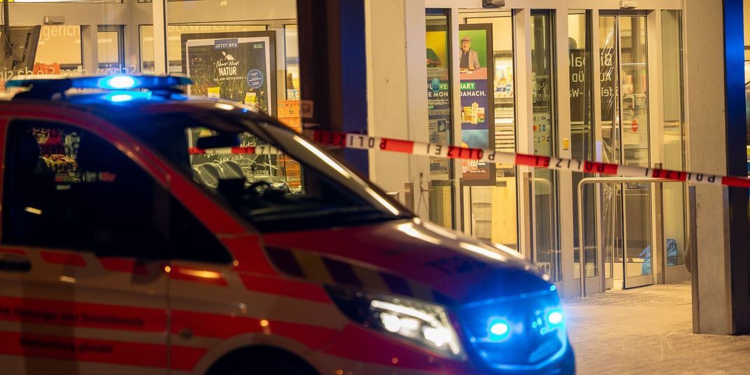 Ein Einsatzfahrzeug steht vor einem Supermarkt mit Blaulicht. Eine Frau wurde in dem Supermarkt erschossen. 