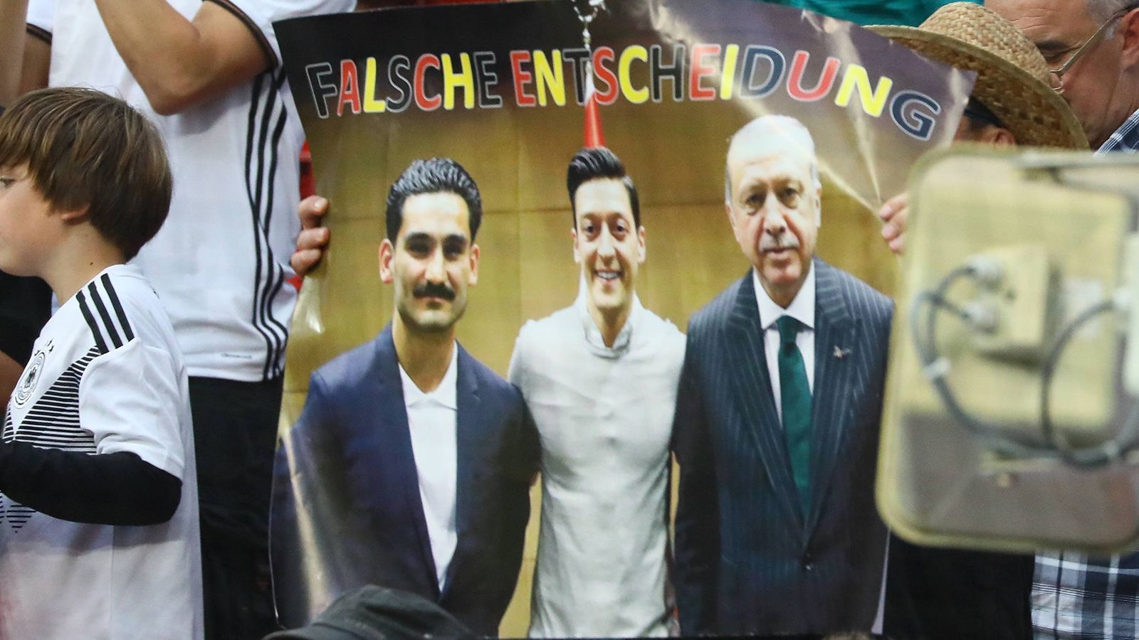 
                <strong>Mesut Özil, Ilkay Gündogan und das Foto mit Recep Tayyip Erdogan</strong><br>
                Kurz vor der WM in Russland sorgten Mesut Özil und Ilkay Gündogan dann für große Diskussionen, weil sie sich mit dem türkischen Präsidenten und Despoten Recep Tayyip Erdogan trafen. Gündogan übergab Erdogan dabei ein Trikot von Manchester City. Darauf stand: "Mit Respekt für meinen Präsidenten." Beide Profis distanzierten sich in der Folge nur halbherzig von Erdogan, wurden dafür weiter kritisiert. Deutsche Fans forderten sogar, dass Özil und Gündogan nicht für das Turnier nominiert werden dürften. Bundestrainer Joachim Löw kam diesen Forderungen nicht nach. Nach der WM wurde auch die Handhabe des DFB stark kritisiert. Für viele Fans ist das Foto "der Anfang vom Untergang" der deutschen Nationalmannschaft.
              