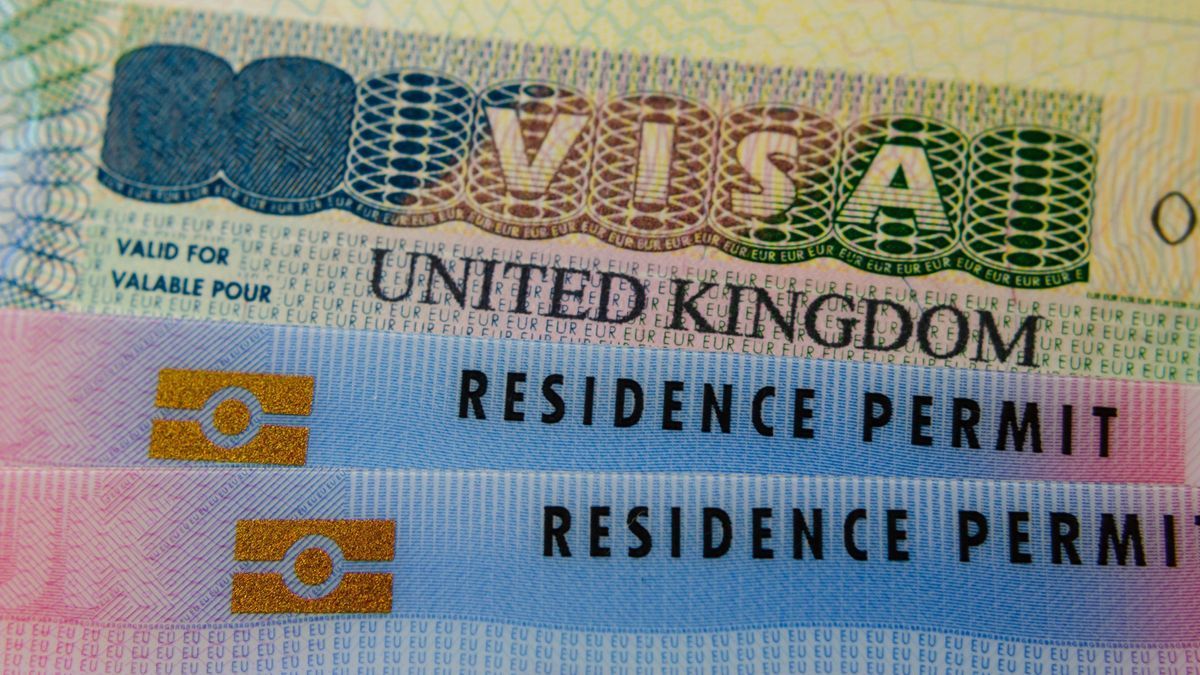 United Kingdom BRP (Biometrical Residence Permit) cards for Tier 2 work visa placed on top of UK VISA sticker in the passport. Close up photo.