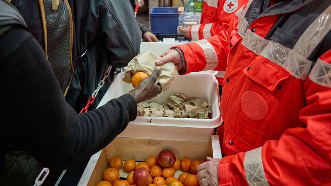 Ehrenamtliche Mitglieder des Deutschen Roten Kreuzes verteilen Lebensmittel an obdachlose Menschen. 