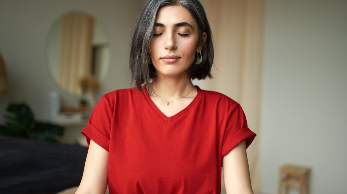 Close up image of beautiful young woman with gray hair and nose ring meditating indoors, using breathing technique, doing pranayamas to prevent stress and level up energy, keeping eyes closed