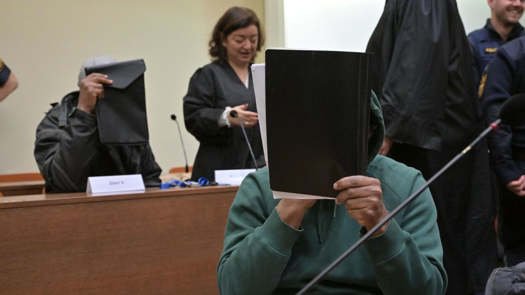 Mutmaßliche Mitglieder der nigerianischen Mafia sitzen zu Prozessauftakt im Gerichtssaal.