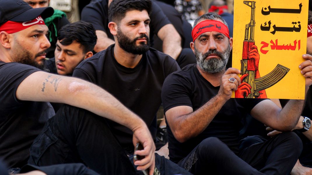 Ein Hisbollah-Anhänger und ein schiitischer Trauernder halten ein Transparent mit der Aufschrift: "Wir werden die Waffen nicht aufgeben" bei einer Massenkundgebung zum Gedenken an Aschura.