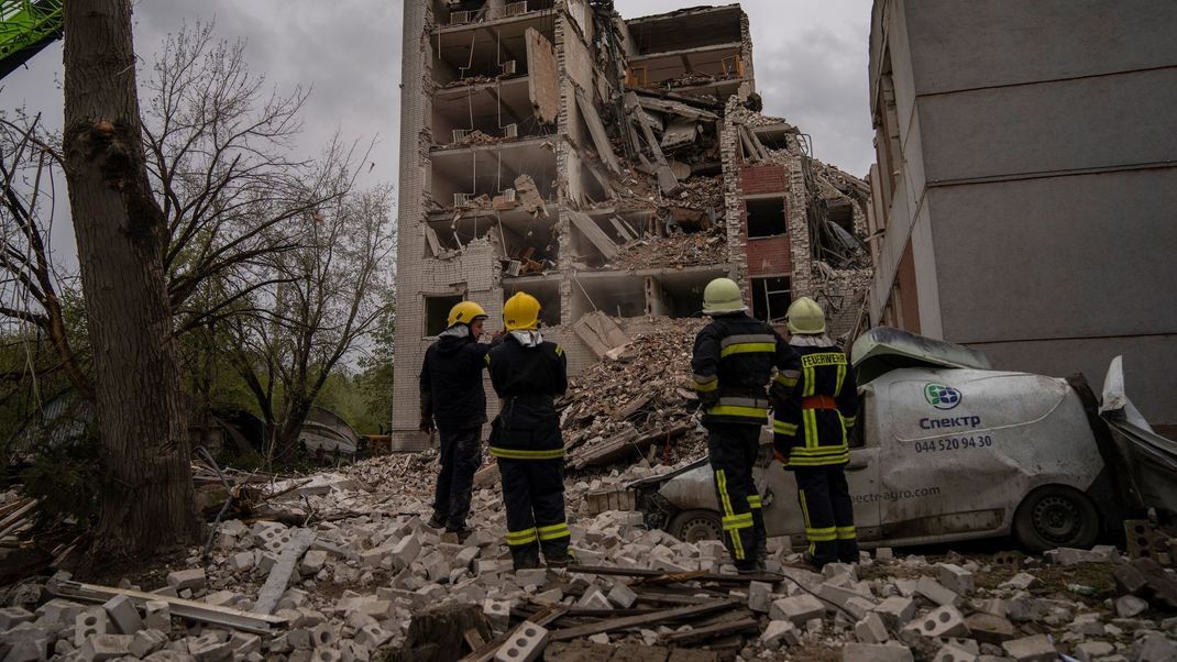 17. April 2024, Ukraine, Tschernihiw: Feuerwehrleute stehen vor einem Gebäude, das durch russische Angriffe stark zerstört wurde.