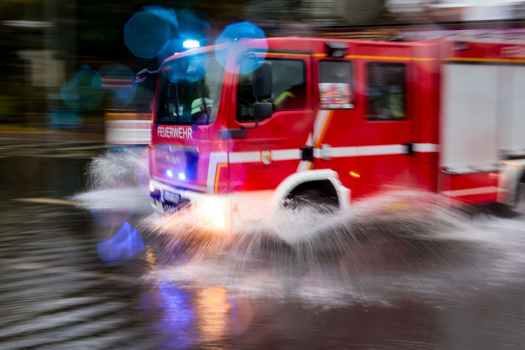 Ein Einsatzfahrzeug der Feuerwehr fährt durch überflutete Straßen.
