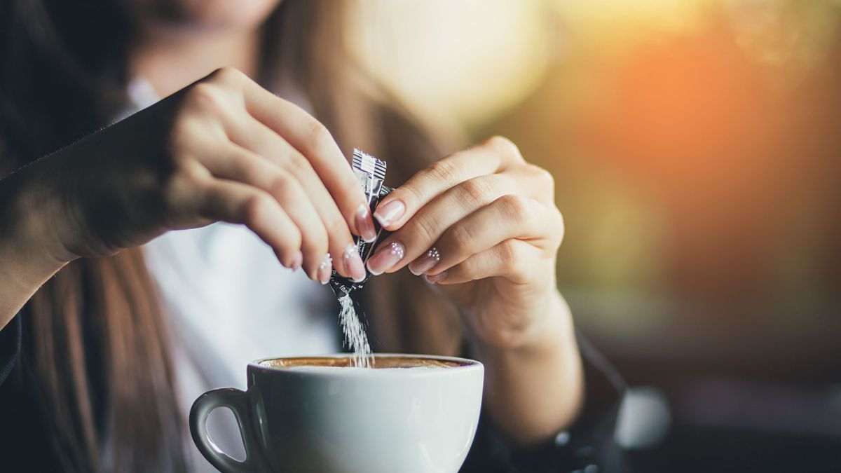 Female hand pours sugar into coffee. Sunlight background