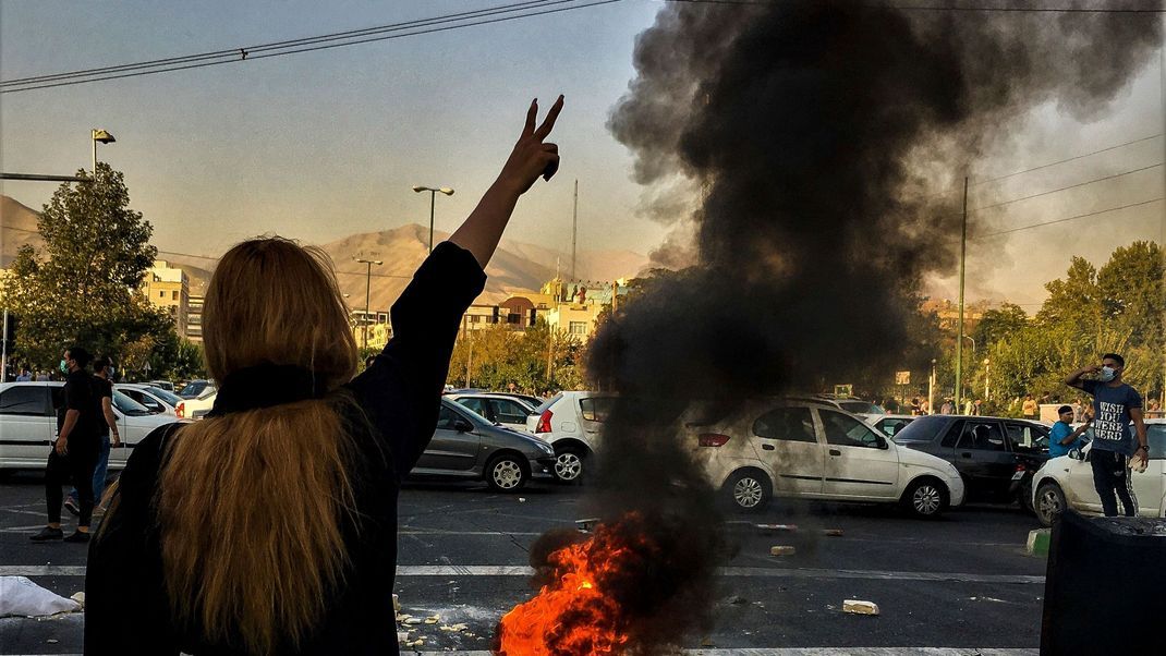 Iran: Eine Frau steht während einer Demonstration nach dem Tod der 22-jährigen Mahsa Amini vor einem brennenden Autoreifen und zeigt das Victory-Zeichen. (Archiv 30.09.2022)