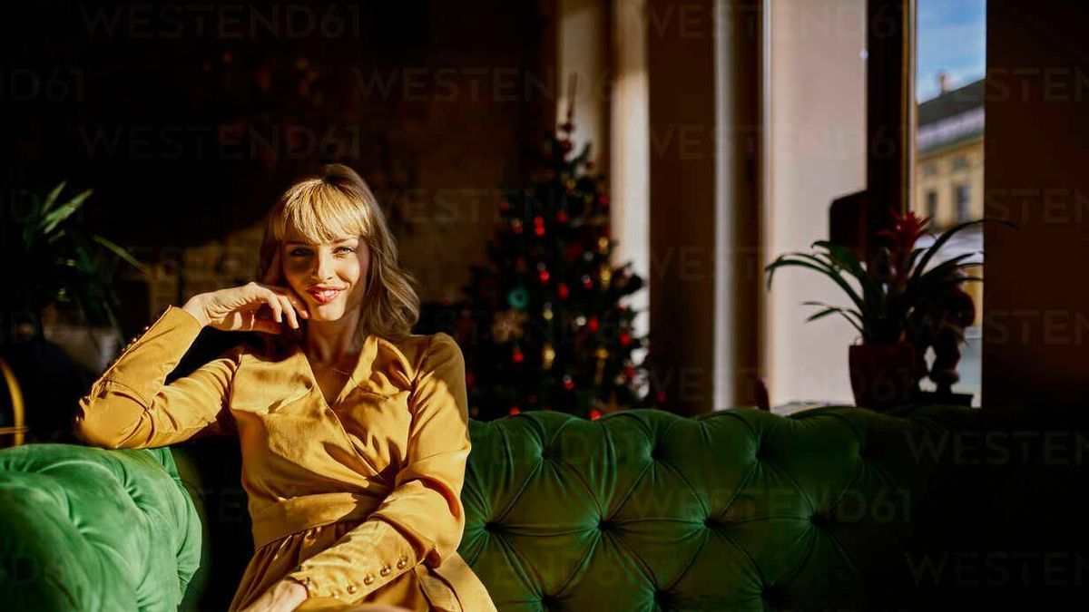ZEDF01153 - Portrait of smiling elegant woman sitting on a couch with Christmas tree in background