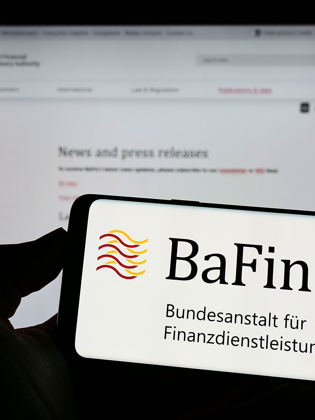 Stuttgart, Germany - 07-15-2022: Person holding cellphone with logo of German financial supervisory authority BaFin on screen in front of webpage. Focus on phone display. 