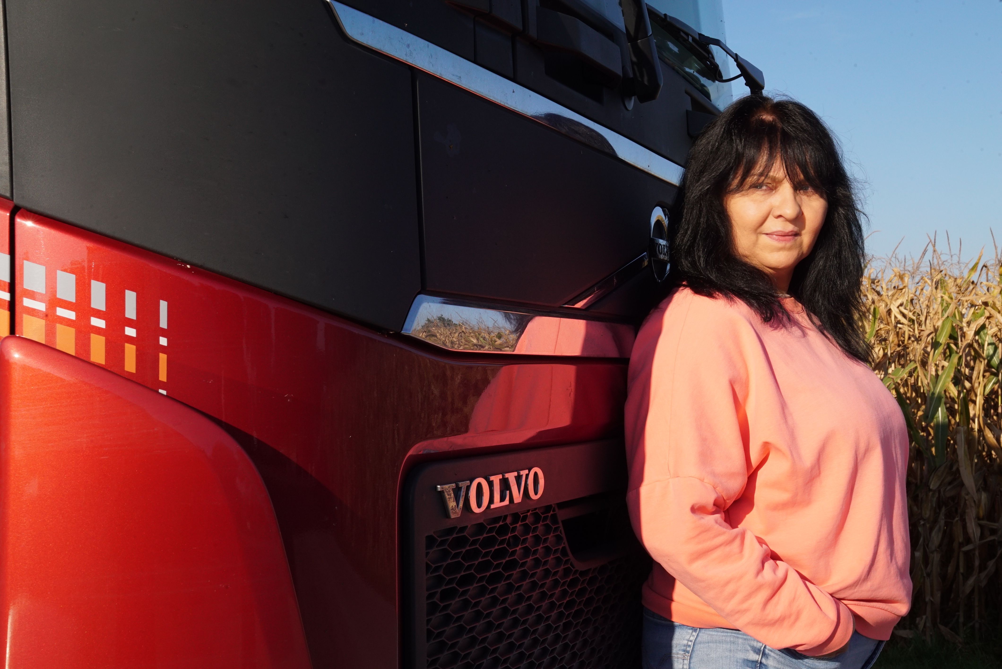 "Trucker Babe" Annette lehnt strahlend an der Fahrerkabine ihres Sattelschleppers mit Auflieger.