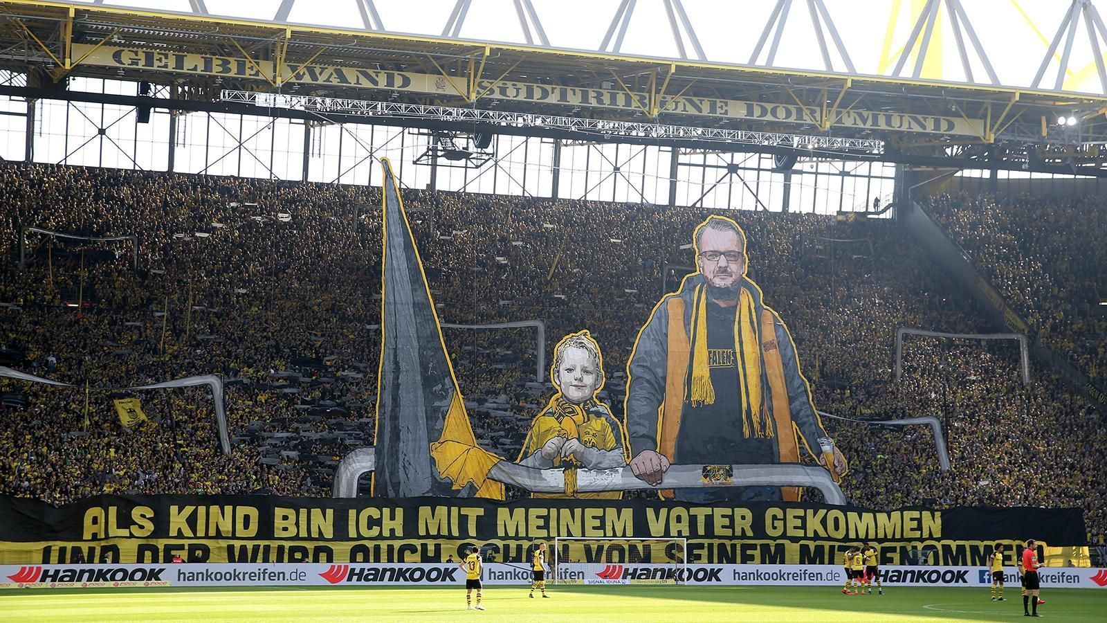 
                <strong>BVB-Choreo gegen Wolfsburg</strong><br>
                Eine beeindruckende Choreographie lieferten die BVB-Fans im Rahmen des 27. Spieltags der Saison 2018/19 gegen den VfL Wolfsburg. "Als Kind bin ich mit meinem Vater gekommen. Und der wurd auch schon von seinem Vater mitgenommen", heißt es auf einem riesigen Banner, über dem zwei BVB-Fans mit Flagge thronen.
              