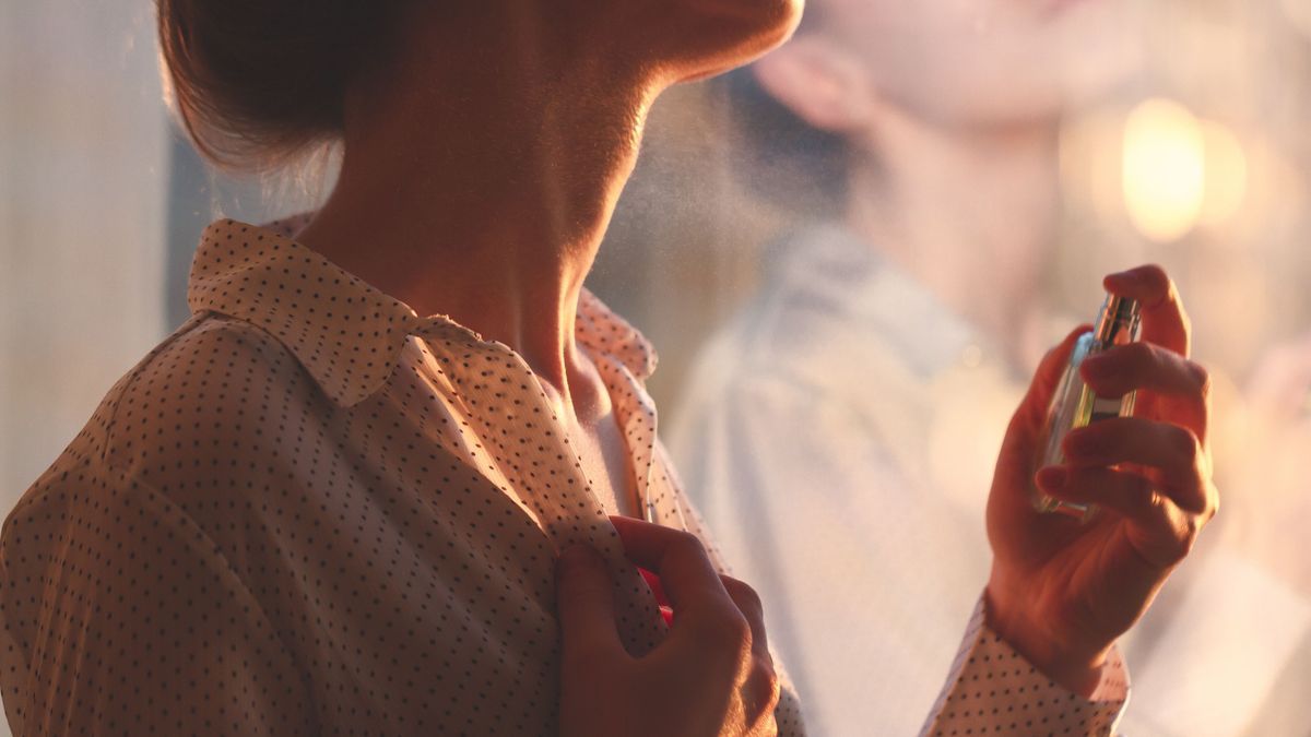 Stylish woman in blouse spraying a bottle of favorite perfume at sunset. Fashion, beauty and style