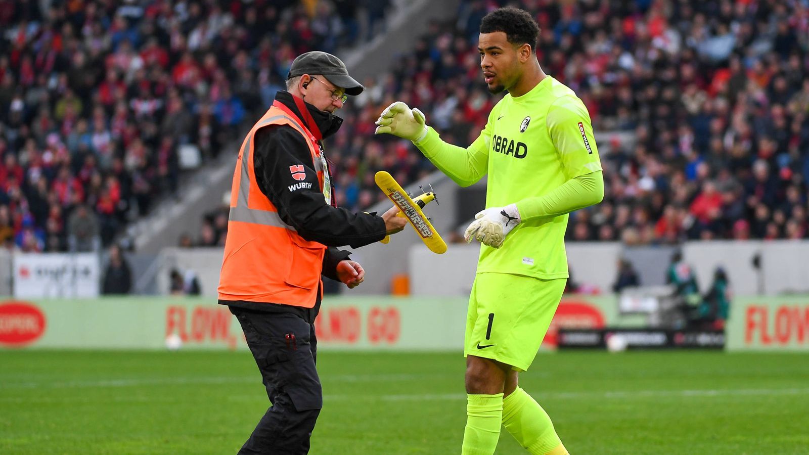 <strong>Keeper Atubolu hilft beim Aufräumen</strong><br>Damit das Spiel möglichst kurz unterbrochen ist, hilft auch Freiburgs Torhüter Noah Atubolu dabei, die auf dem Rasen gelandeten Flugzeuge zu entfernen.&nbsp;