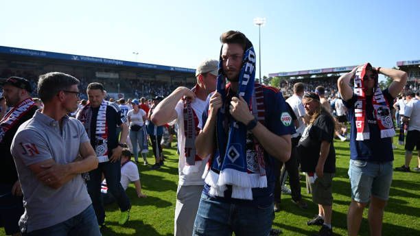 <strong>Saison 2022/23 - 34. Spieltag</strong><br>Am letzten Spieltag der Saison spielt sich die wohl tragischste Szenerie der jüngeren Vereinsgeschichte beim HSV ab. Auf Minuten der Ekstase folgen Schock, Trauer und Schmerz. Mit einem 1:0 setzt sich der HSV gegen Sandhausen durch. Nach Abpfiff stürmen die Fans den Platz: Es heißt Aufstieg. Wenige Minuten später dann Ernüchterung. Heidenheim dreht das Spiel in Regensburg durch zwei Treffer in der Nachspielzeit und schiebt sich an den Rothosen vorbei. Der HSV muss erneut in die Relegation.