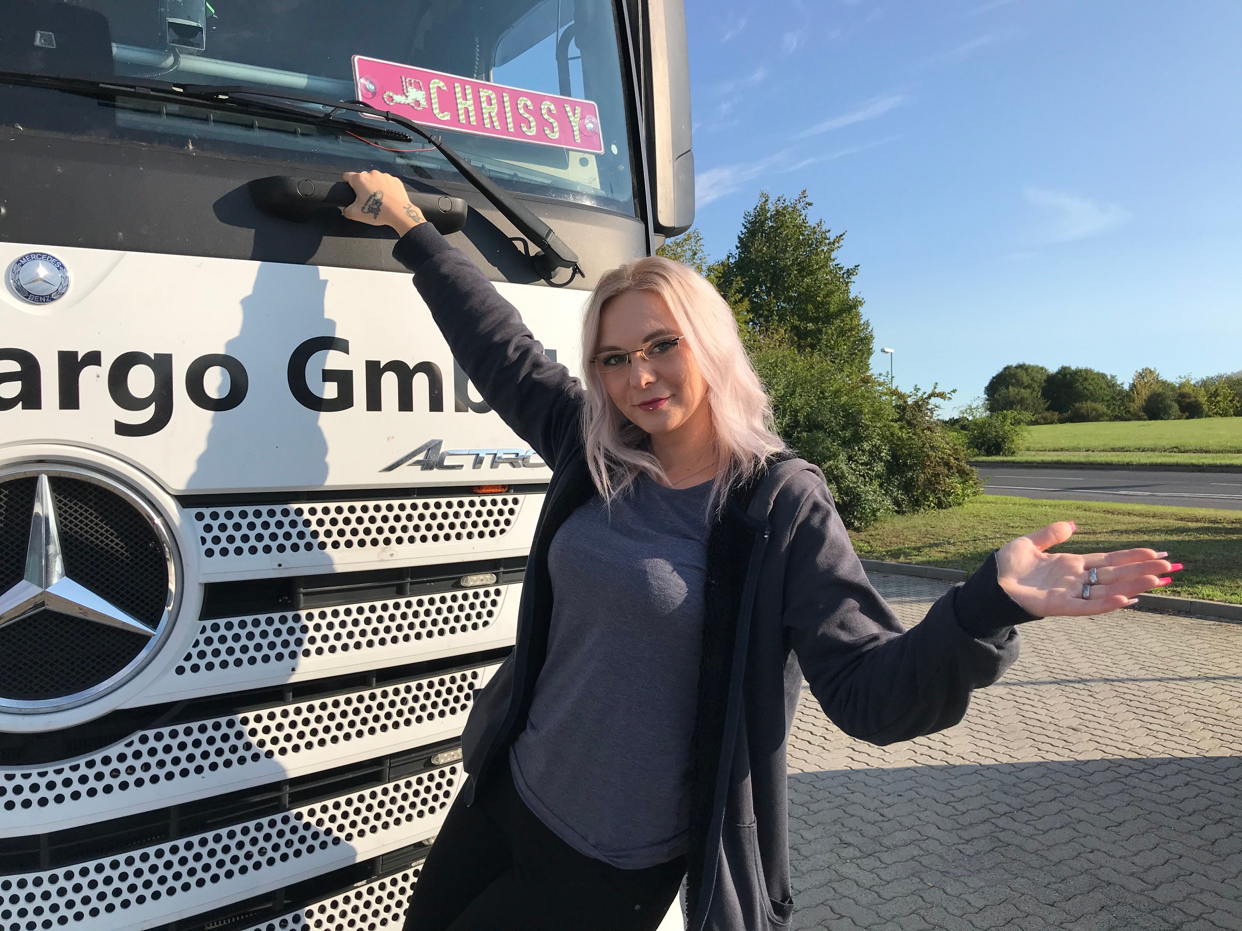 Vor einem weißen Truck befindet sich "Trucker Babe" Chrissy.
