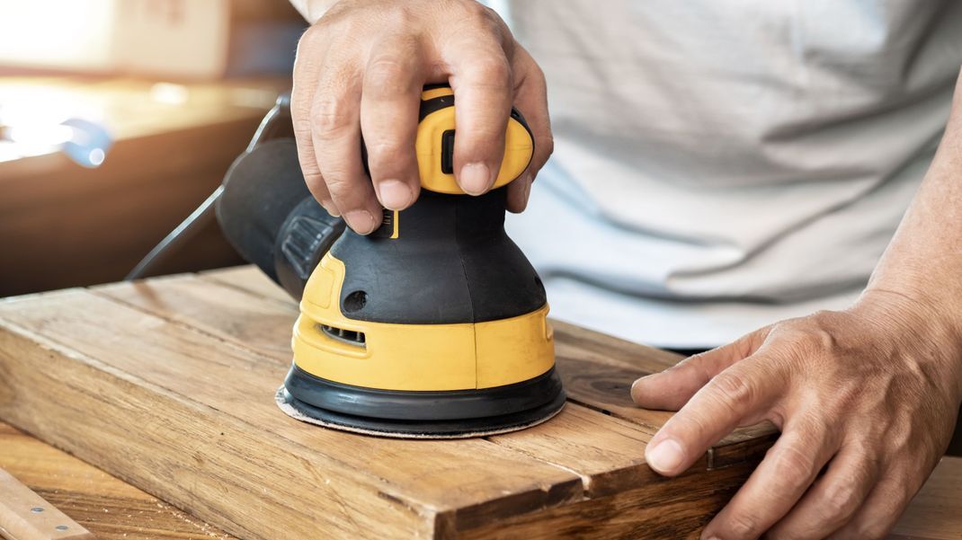 Handwerker glättet mit dem Exzenterschleifer eine Holzoberfläche.