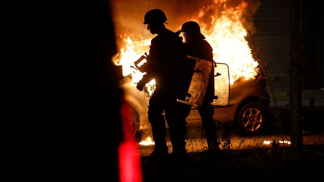Bereitschaftspolizisten stehen in der Nähe eines brennenden Autos im Viertel La Meinau. 