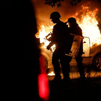 Bereitschaftspolizisten stehen in der Nähe eines brennenden Autos im Viertel La Meinau. 