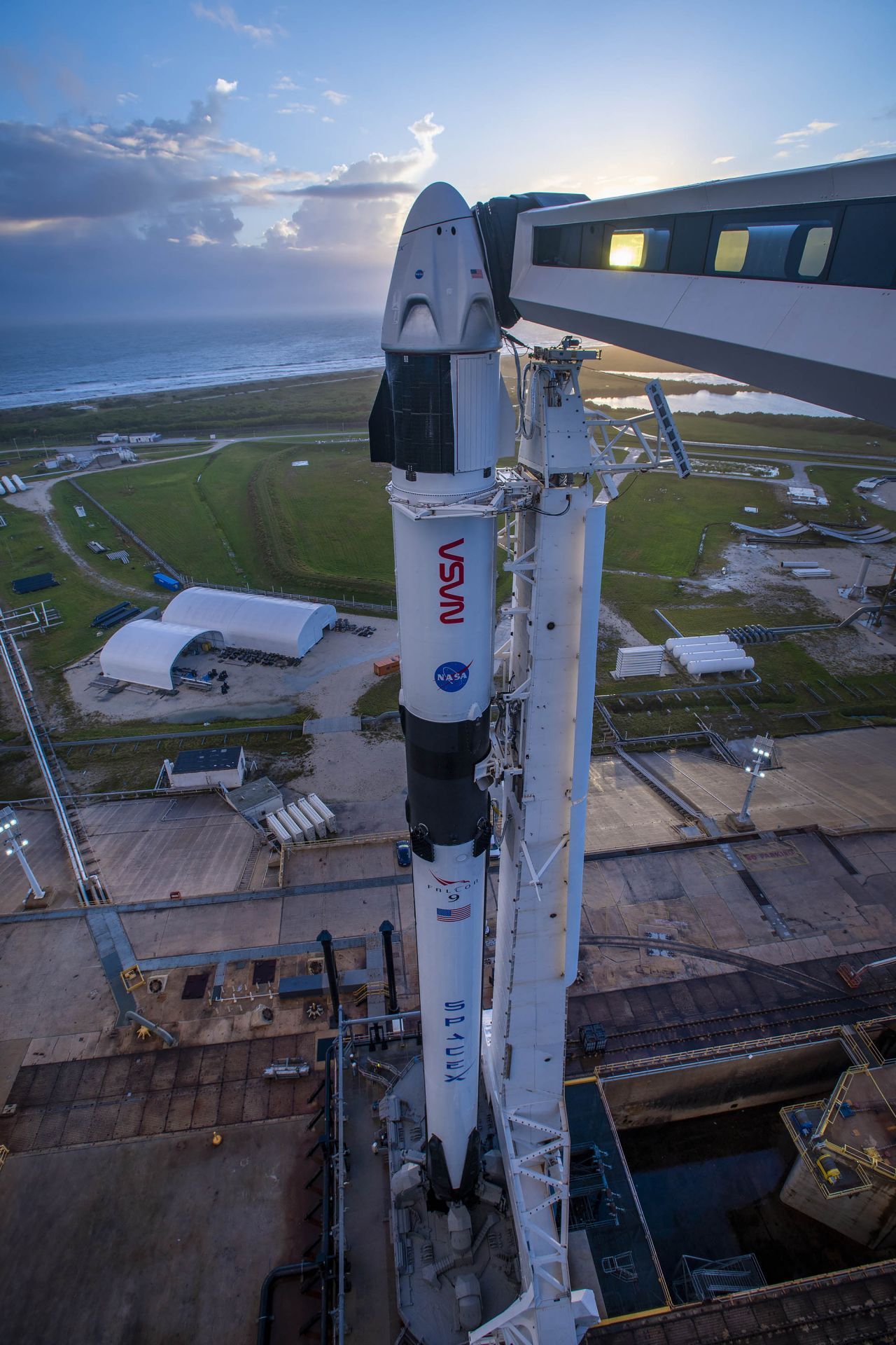 Der Crew Dragon auf der Spitze einer Falcon-9-Rakete montiert. Über den Arm gelangen die Astronauten und Astronautinnen ins Raumschiff. Er wird später zurückgeklappt, so dass die Rakete beim Starten freie Bahn hat.   