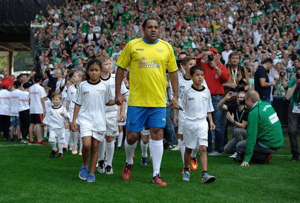 
                <strong>Los geht's!</strong><br>
                Ailton, der Kugelblitz aus Brasilien, versammelt zum Abschiedsspiel seine ehemaligen Mitstreiter im Weser-Stadion. Wie es sich gehört, wird er von zwei Einlaufkindern aufs Feld begleitet.
              