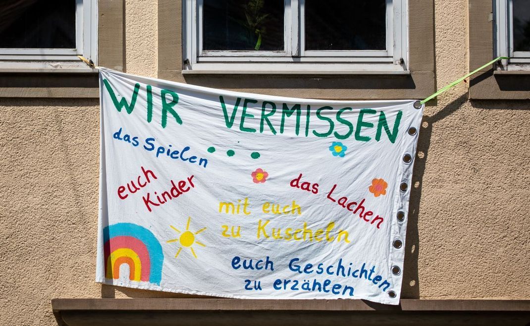 "Wir vermissen das Spielen, das Lachen, euch Kinder, mit euch Kuscheln und mit euch Geschichten erzählen" steht auf einem großen Banner an der Fassade eines Kindergartens in Baden-Württemberg.