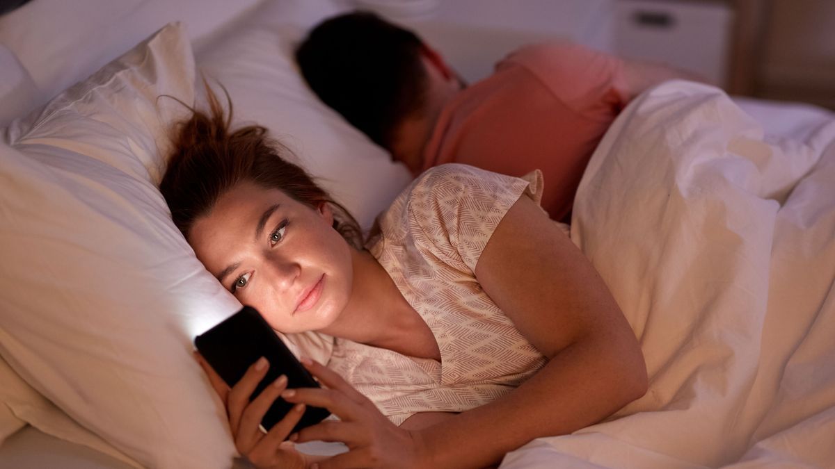 Frau ist am Handy, während ihr Partner neben dran schläft.