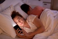Frau ist am Handy, während ihr Partner neben dran schläft.