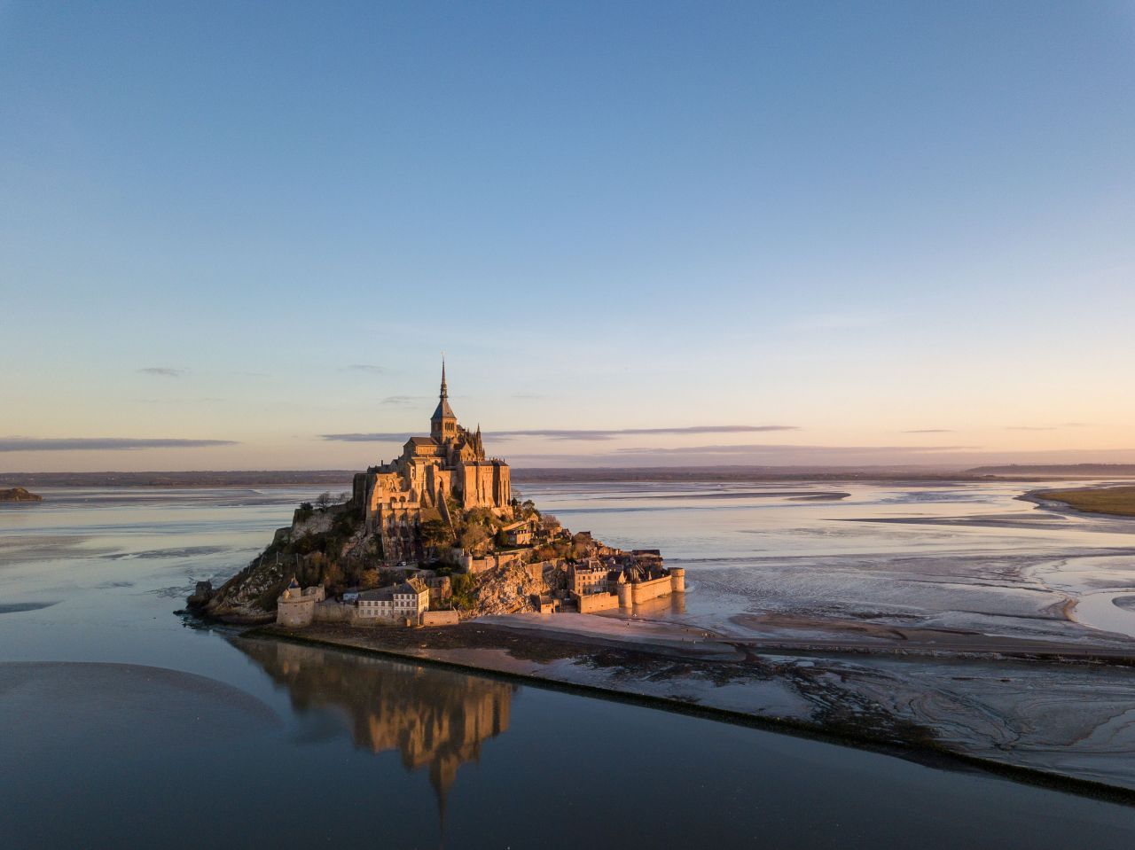 Der Mont Saint-Michel in der Normandie ist eine kleine Insel, die bei Flut von Wasser umgeben ist und bei Ebbe auf einem sandigen Untergrund steht. Die Gezeiten hier ändern die gesamte Umgebung und bietet ein beeindruckendes Schauspiel.