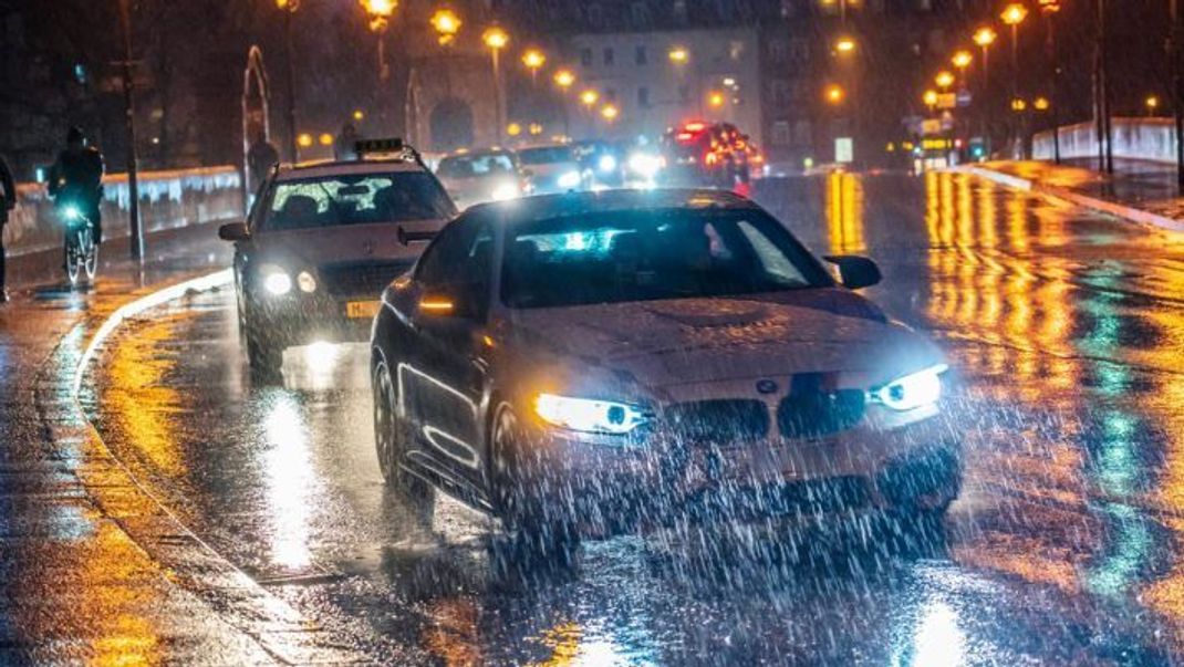 Autos fahren bei Regen und Dunkelheit mit Abblendlicht über die Wittelsbacher Brücke in München.