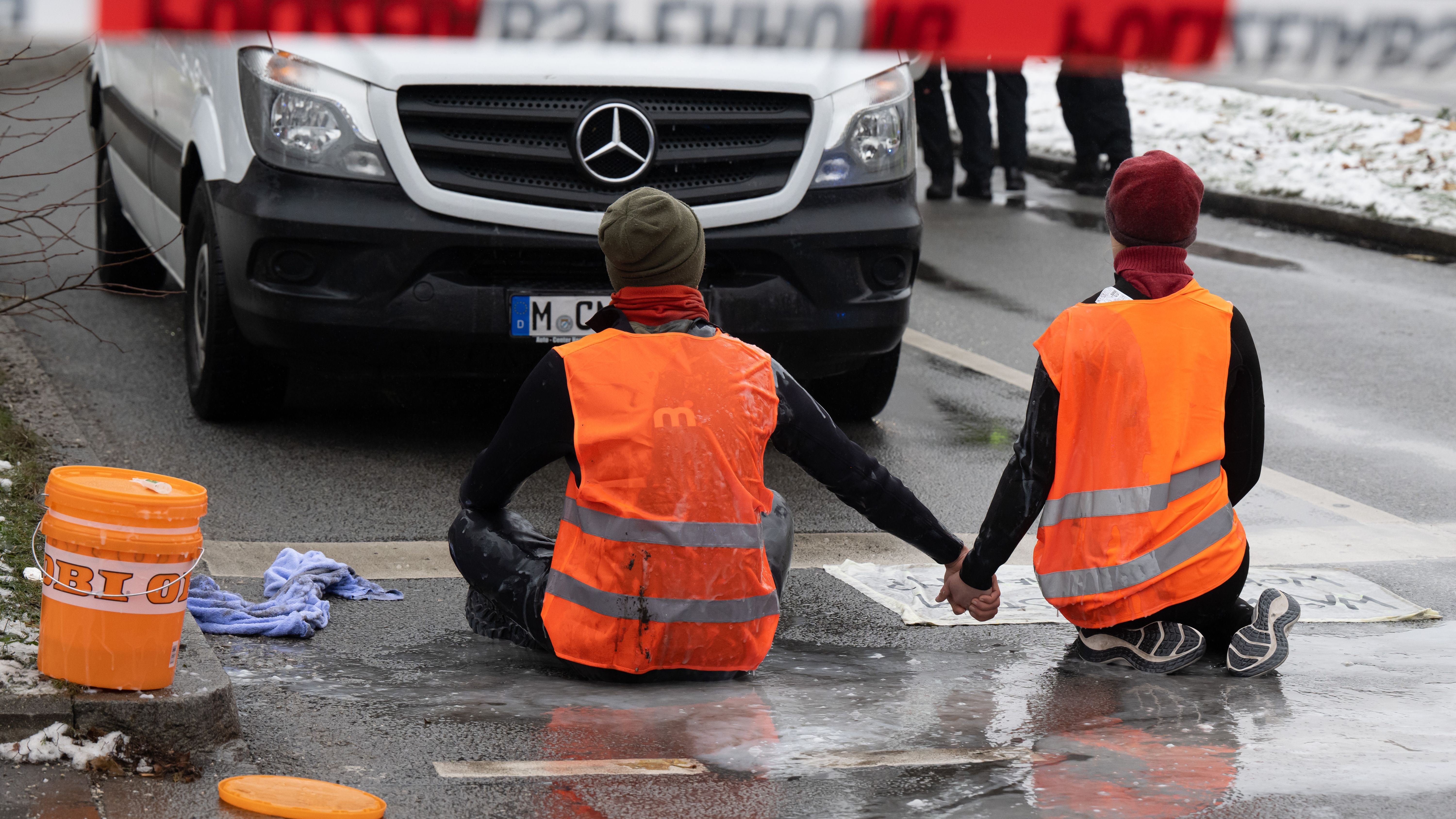 Zwei Klimaaktivisten nehmen an einer Protestaktion der Gruppe "Letzte Generation" teil, indem sie versuchen sich auf einer Strasse trotz Nieselregen und Minusgraden festzukleben. 