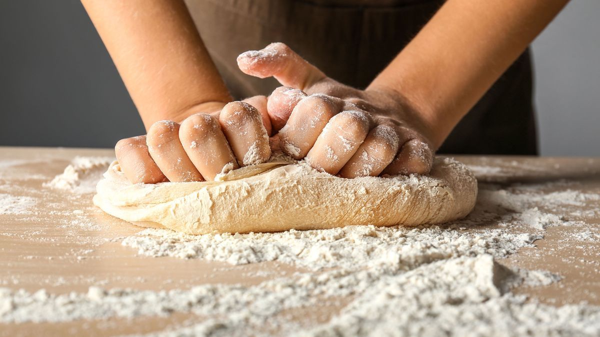 Frau knetet Teig auf einem Holzbrett