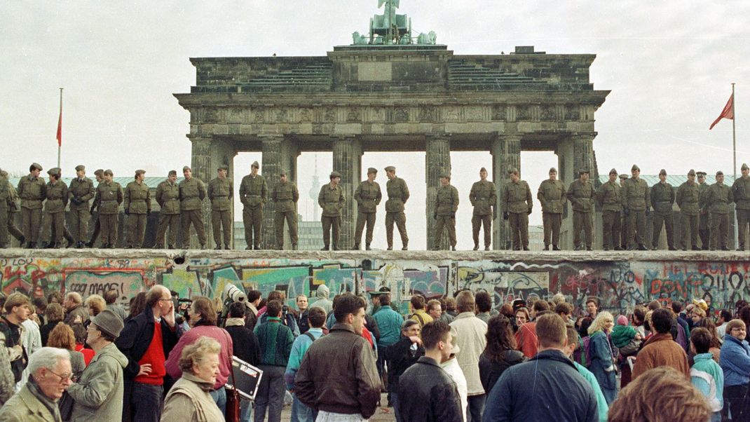 Ostberliner Grenzsoldaten stehen auf der Berliner Mauer vor dem Brandenburger Tor