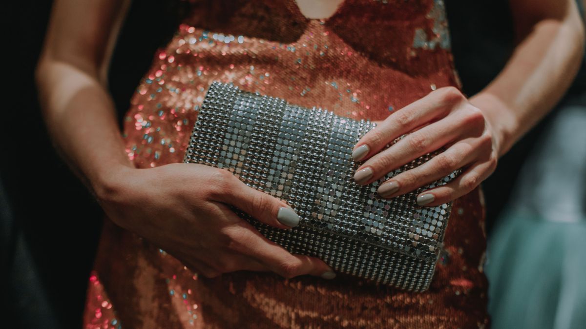Female hands holding a small metal silver handbag. Female fashion, stylish details