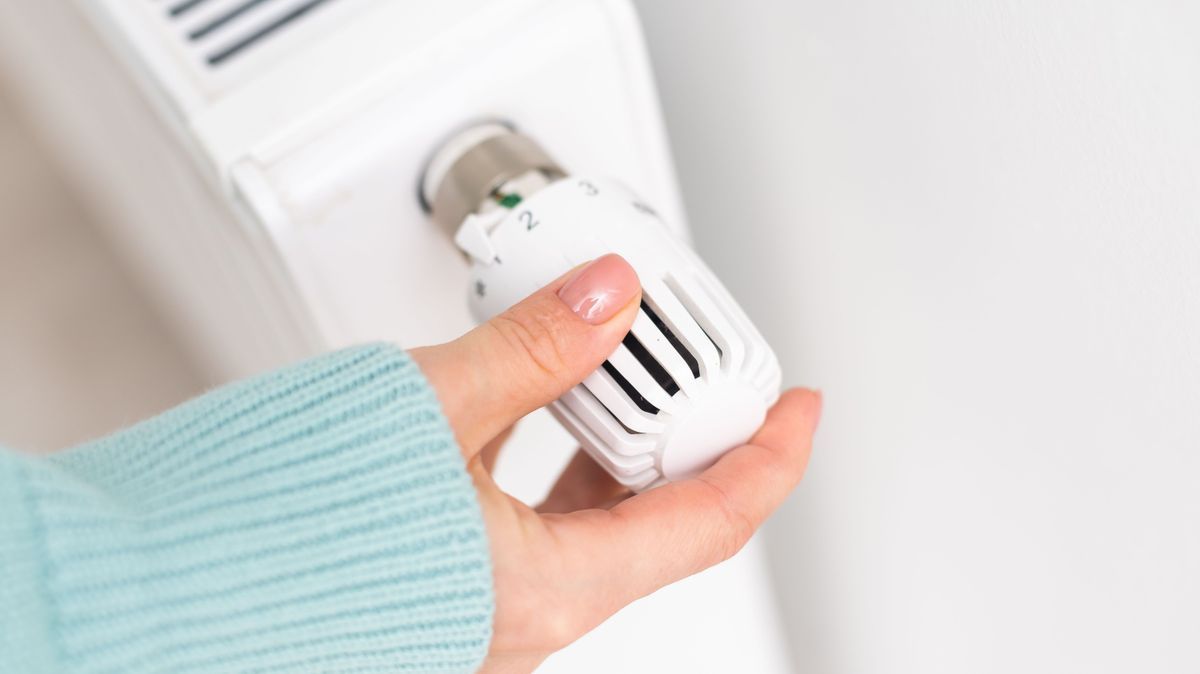Hand einer Frau reguliert Temperatur an der Heizung Energie sparen im Winter beim Lüften