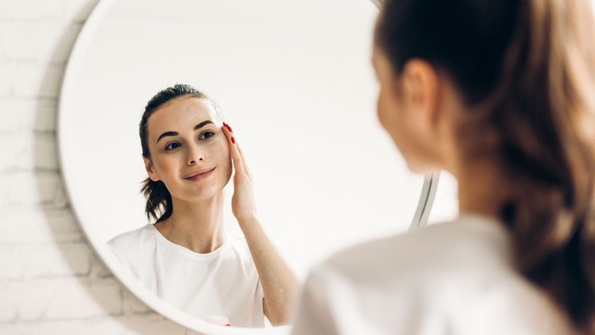 The woman is making up in the bathroom. Woman in bathroom applying cream on face.