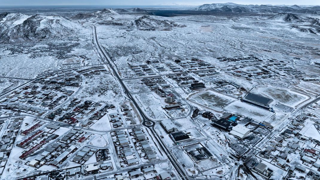 21.12.2023, Island, Grindavik: Das Lavafeld, das durch die jüngste vulkanische Aktivität entstanden ist, ist im oberen Hintergrund über Grindavik auf der isländischen Halbinsel Reykjanes zu sehen. 