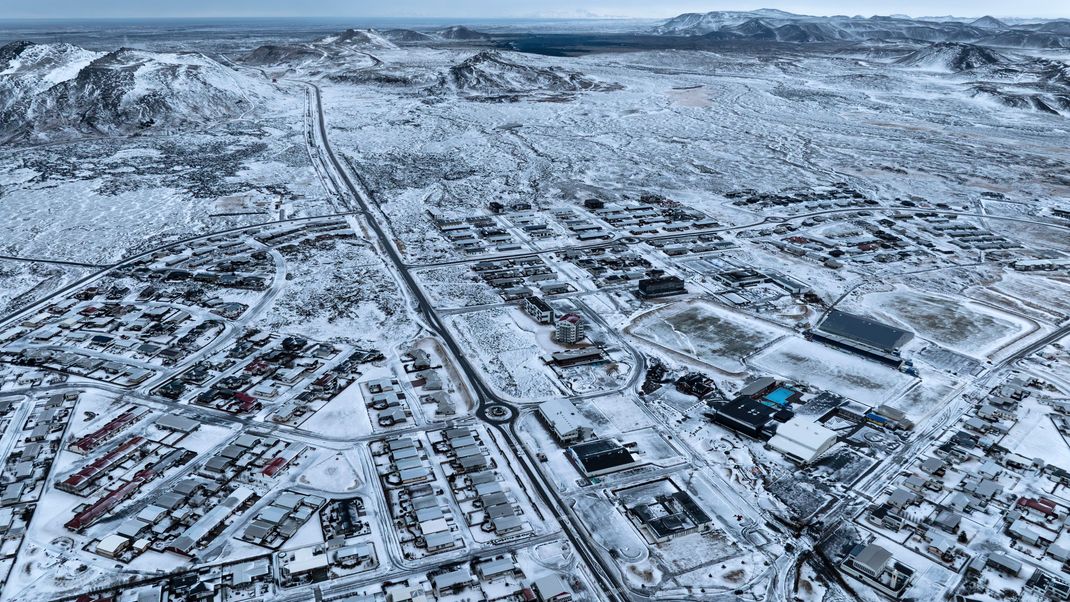 21.12.2023, Island, Grindavik: Das Lavafeld, das durch die jüngste vulkanische Aktivität entstanden ist, ist im oberen Hintergrund über Grindavik auf der isländischen Halbinsel Reykjanes zu sehen. 