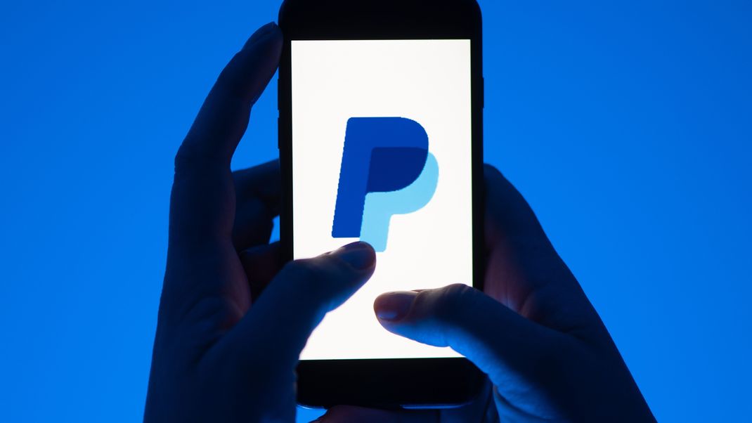 Eine Frau hält ein Smartphone mit dem Logo des Bezahldienst PayPal.
